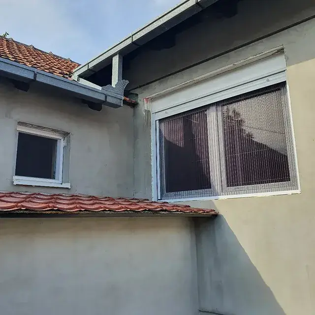 Prozor sa roletnom i komarnikom ispod krovnog venca kuće
