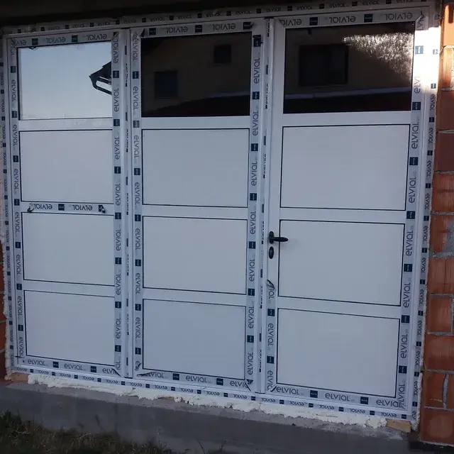 Bela PVC garažna vrata ugrađena na objektu od cigle
